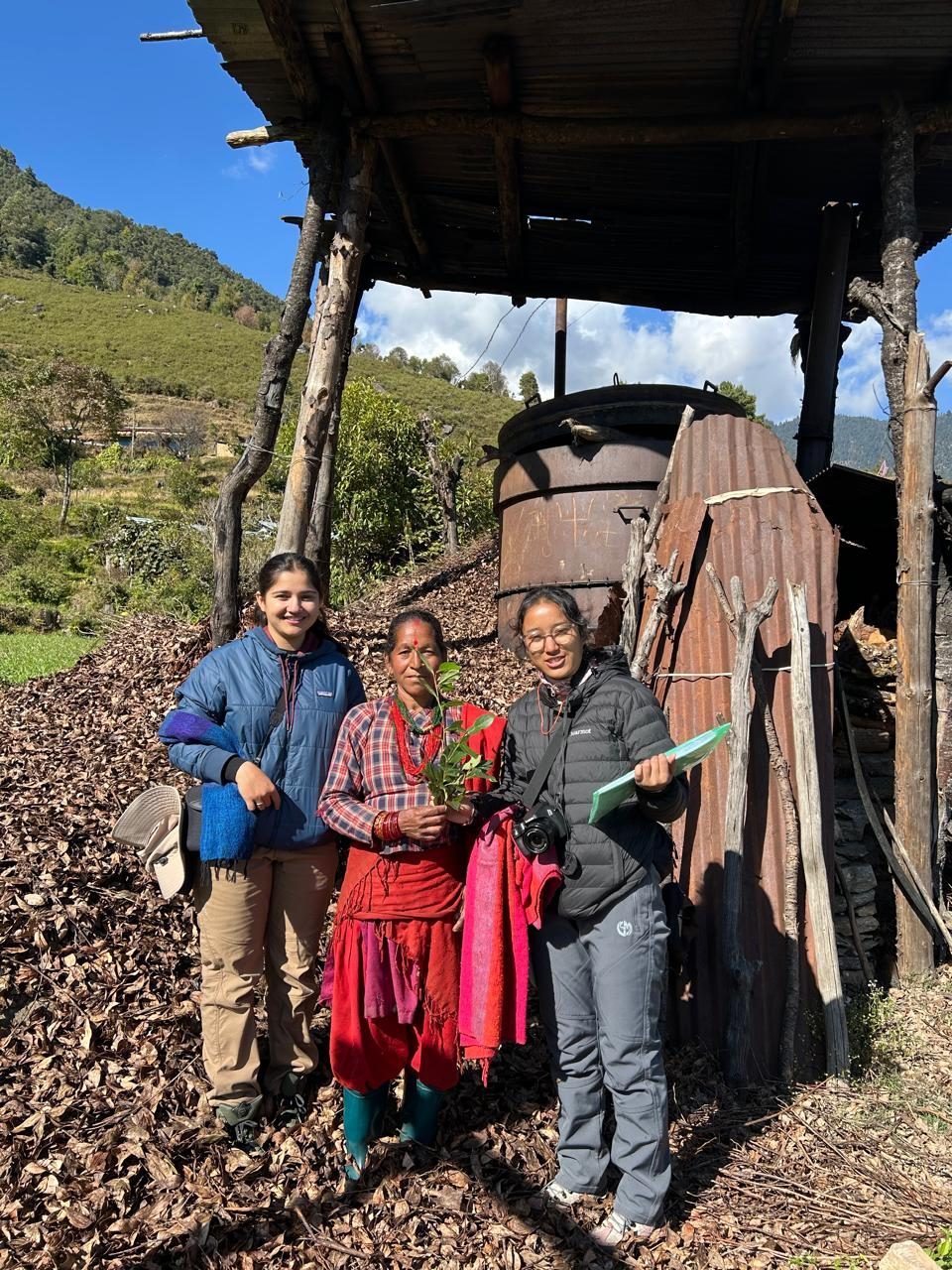 Abhishu Neupane and Shejal Pradhan with a farmer holding a seedling beside an essential-oil still